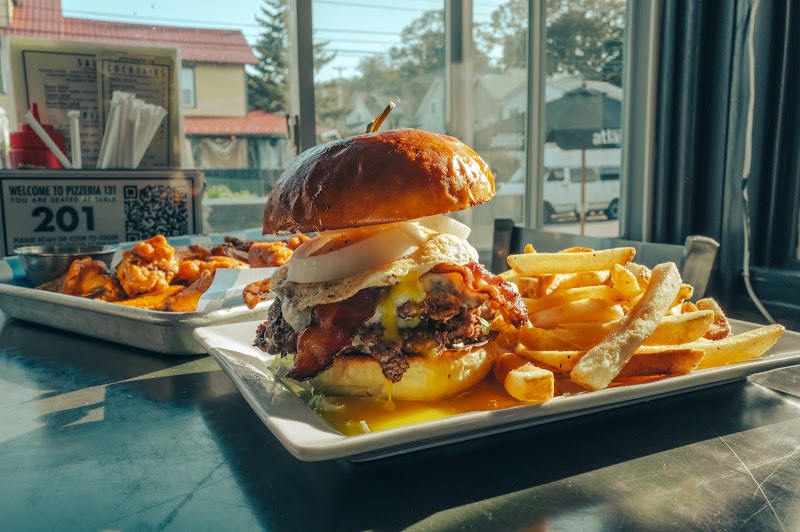 Juicy cheeseburger with melted cheese, onions and crispy bacon, plus thick fries on a white plate near a window at Acadia National Park.
