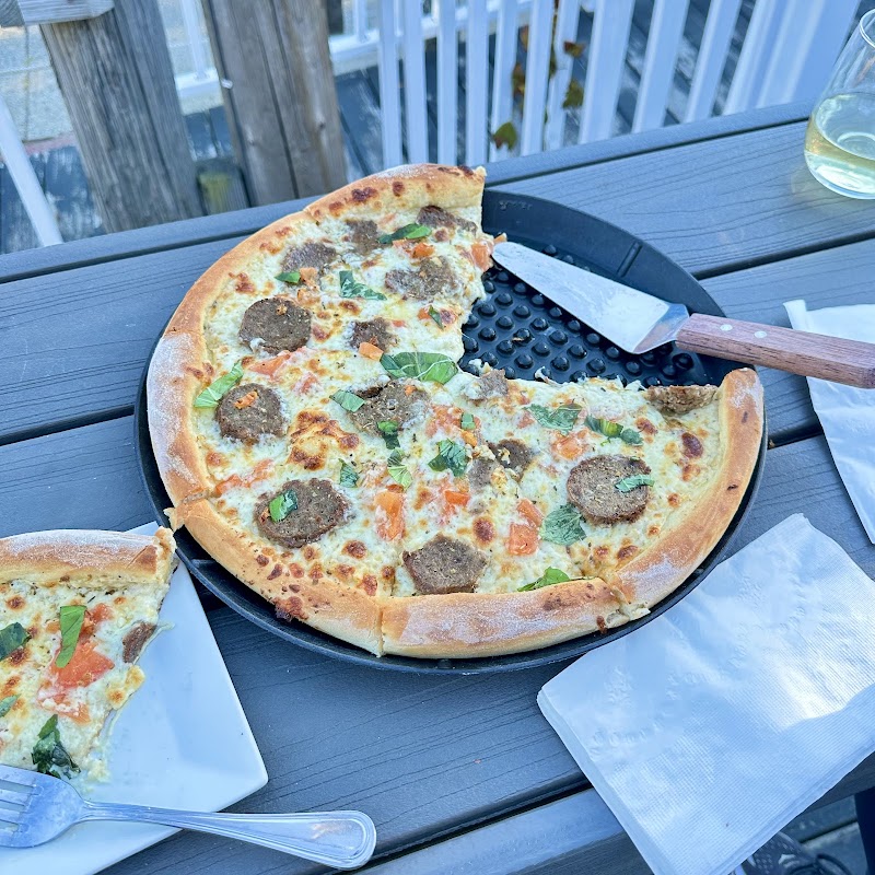 Pizza on a round pan with meatballs and basil rests on a wooden table; wine glass nearby in Acadia National Park.
