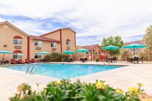 Outdoor pool area with beige two-story motel buildings, turquoise umbrellas, and seating under blue skies at Arches National Park.