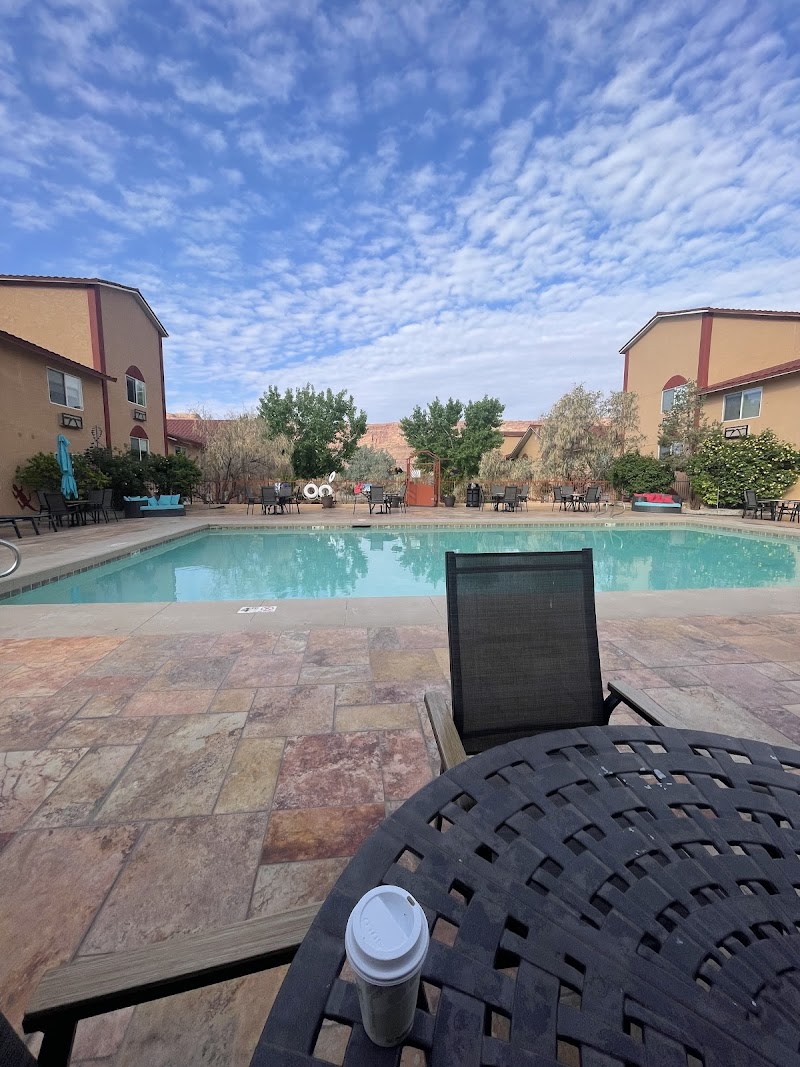 Arches National Park lodge pool area with a turquoise rectangular pool, lounge chairs, umbrellas, and a lattice table with a takeaway cup in front.