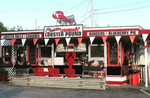 Red-and-white lobster shack with triangular pennants, red Adirondack chairs, and chalkboard menus in Acadia National Park