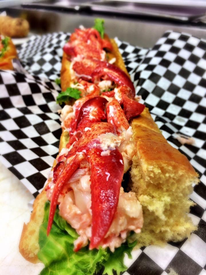 Lobster roll with bright lobster meat on a toasted bun, greens underneath, set on checkered paper in Acadia National Park.
