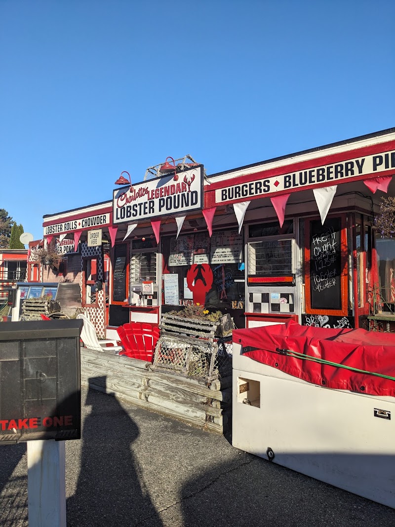 Bright blue sky over a red-and-white lobster pound building in Acadia National Park, with bunting, chalkboard menus, crates, and a large lobster sign.