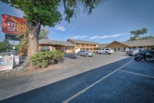 Lodge-style lodging exterior in Yellowstone National Park, with a gravel lot and green trees surrounding the building.