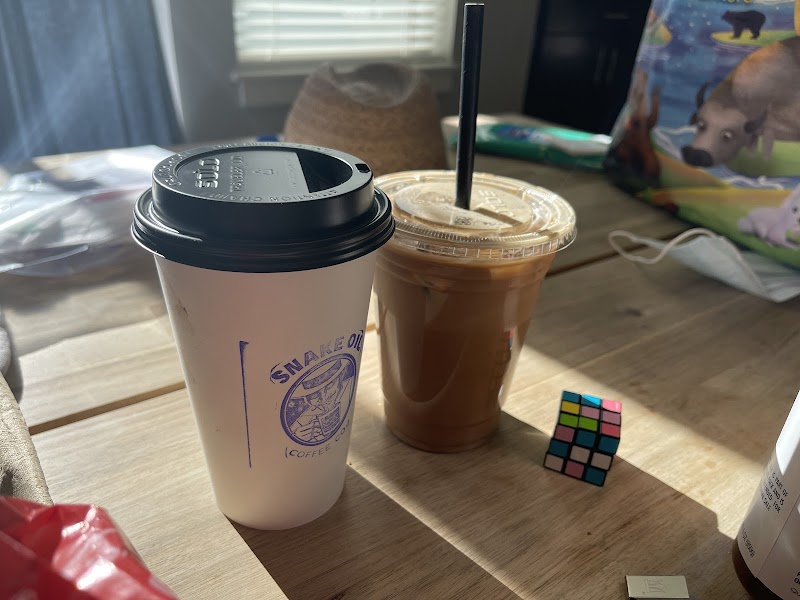 Coffee cups on a wooden table in Arches National Park, including a hot white-cup coffee and an iced beverage with a straw.