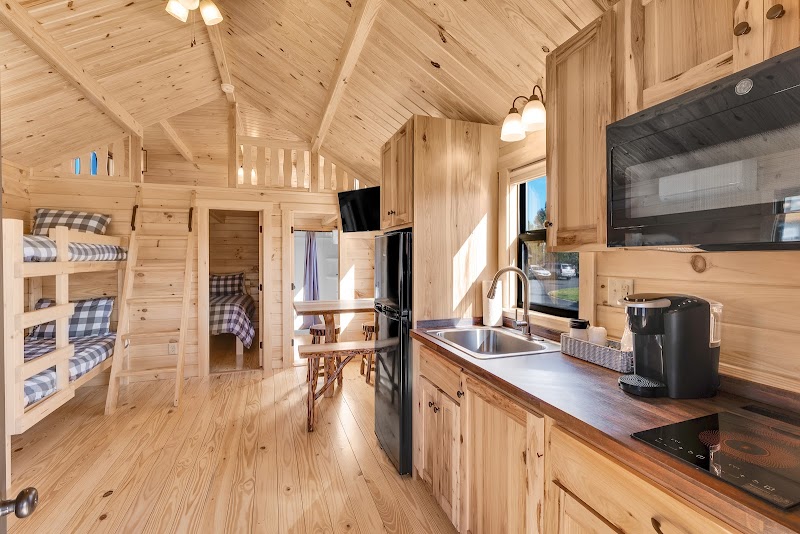 Wood-paneled cabin interior with bunk beds, a compact kitchen, table and chairs, and a window in Yellowstone National Park.