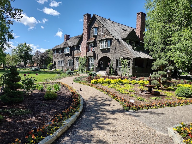 Stone mansion with arched entry, manicured garden beds, winding gravel path, and a fountain in Glacier National Park. — June