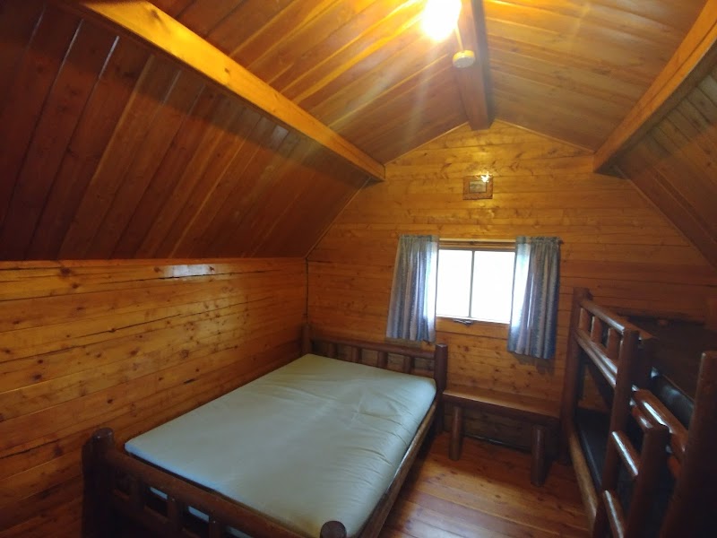 Cozy wooden cabin interior with a bed on the left, bunks on the right, and a small window in Badlands National Park.