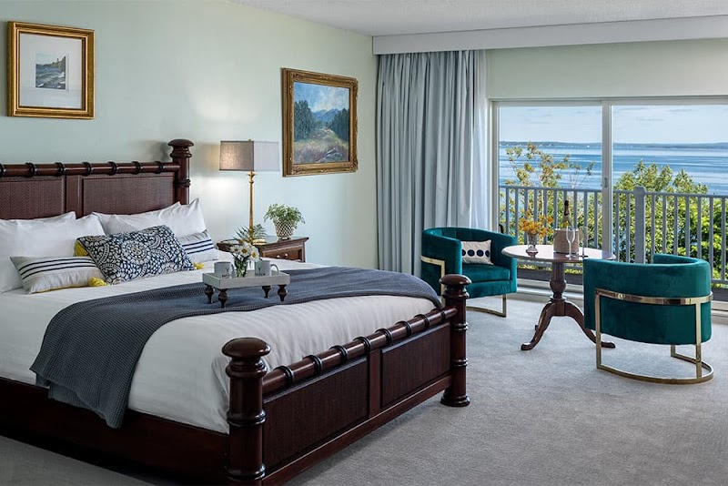 Luxurious hotel room with a dark wood four-poster bed, teal chairs, and an ocean-view balcony at Acadia National Park.
