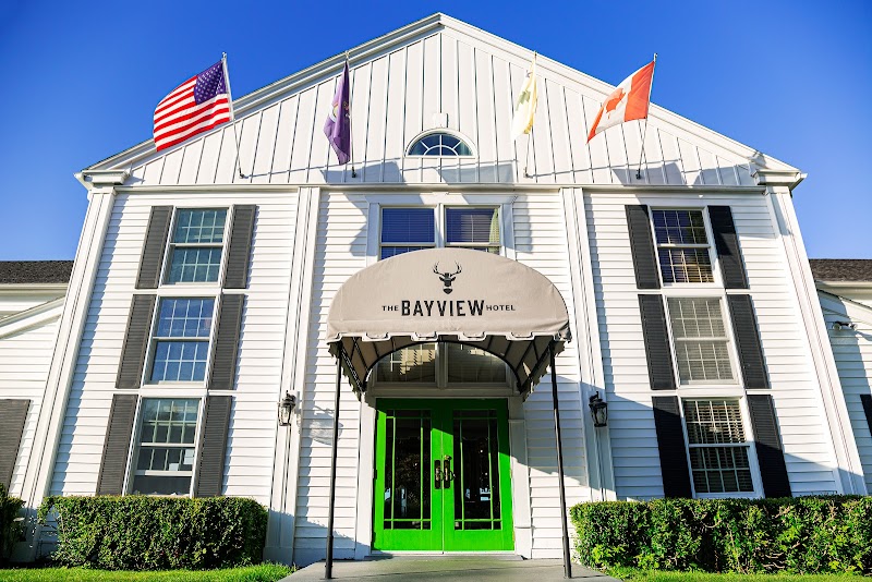 White hotel building with a bright green double door under a curved awning, flags atop, and trimmed hedges in Acadia National Park.