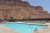 Poolside scene at a lodge with sun loungers, a blue swimming pool, and red rock cliffs in Arches National Park.