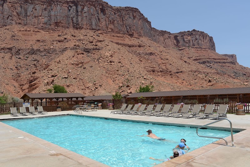 Poolside scene at a lodge with sun loungers, a blue swimming pool, and red rock cliffs in Arches National Park.