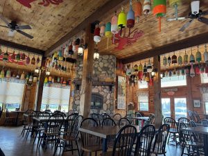 Rustic restaurant interior in Acadia National Park, decorated with colorful hanging buoys and a stone fireplace centerpiece.