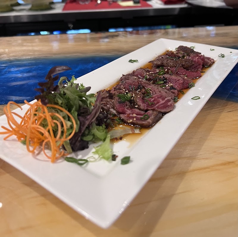 Thinly sliced beef tataki arranged on a white plate with greens and carrot ribbons in a restaurant setting inside Acadia National Park.