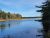 Calm lake with forested shoreline and a clear blue sky in Acadia National Park, autumn colors along the edge.