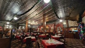 Interior of a Yellowstone dining hall decorated with garlands and string lights, red tablecloths and chandeliers.