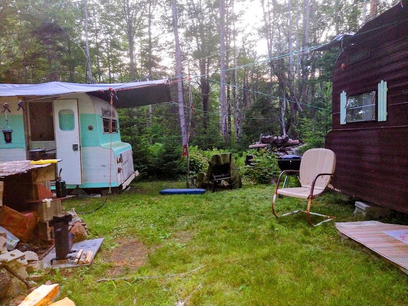 Stockton Springs campsite scene in Acadia National Park with a vintage trailer, chairs, and woodland surroundings.