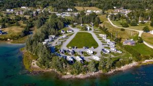 Campground at Acadia National Park with numerous RVs and trailers parked around a grassy central loop by the shoreline.