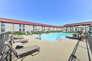 Outdoor pool at Cody lodging near Yellowstone National Park, with sun loungers, umbrellas, and a fenced patio under a clear blue sky.