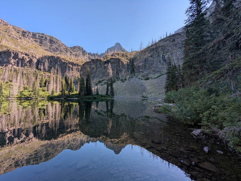 Snyder Lake at Glacier National Park reflects surrounding cliffs and pine shoreline.