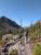 Hiker with a green backpack treks a rocky trail toward Snyder Lake Campground in Glacier National Park.