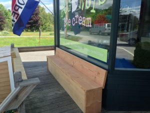 A wooden bench sits outside a bright ice cream shop window along a park road in Acadia National Park.