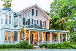 Elegant white two-story inn with a wraparound porch, columns, and warm glowing windows in Acadia National Park.