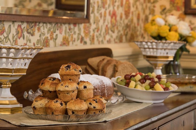 Stack of blueberry muffins on a glass tray, loaf of bread, and a fruit bowl with grapes on a counter in Acadia National Park.