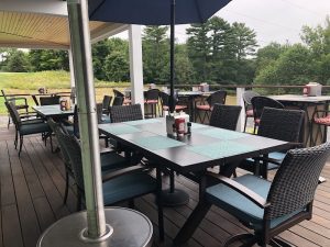 Outdoor restaurant patio on a wooden deck with wicker chairs and umbrellas in Acadia National Park.