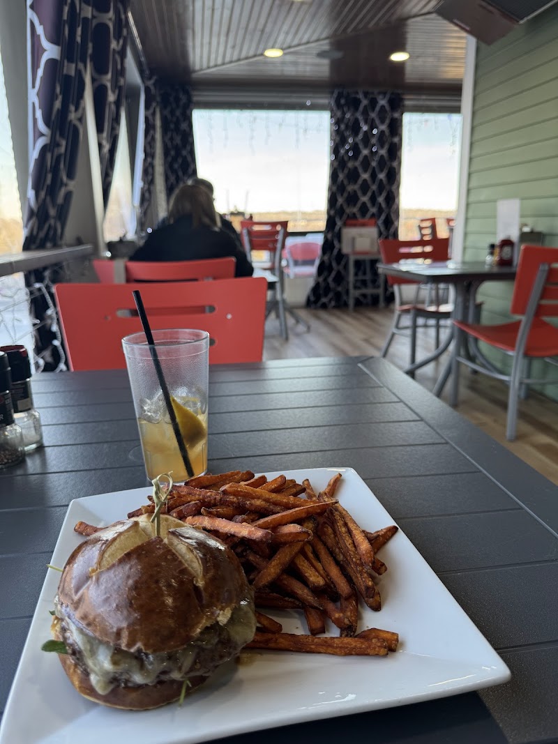 Inside a casual cafe at Acadia National Park, a cheeseburger with melted cheese and a side of fries on a square plate with a glass of lemonade nearby.