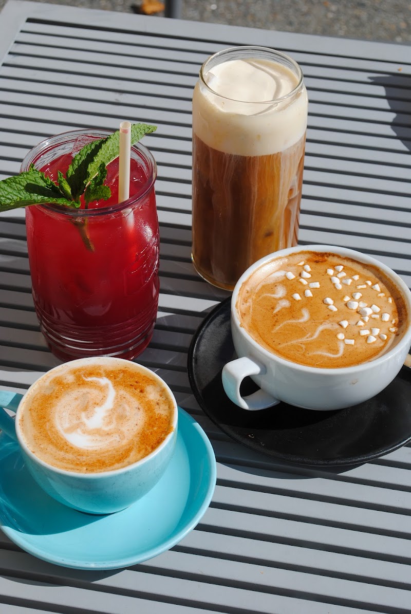 A park cafe table scene in Acadia National Park featuring a white cup of latte, a blue cup with latte art, and two iced beverages in tall glasses.