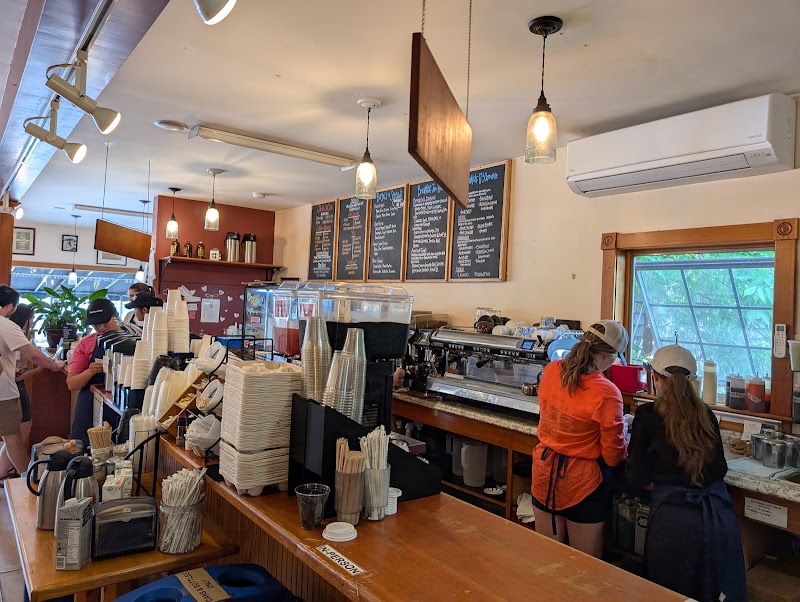 Inside a cozy cafe in Acadia National Park, coffee bar with cups, grinders, and customers at the counter.