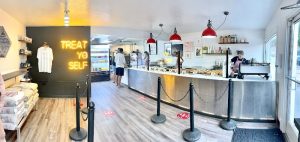 Inside a modern cafe at Arches National Park, a long curved counter with red pendant lights, pastries, and customers ordering.