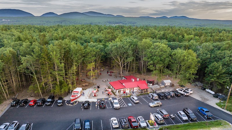 Aerial view of a red-roofed restaurant amid tall pines, a busy parking lot, and dense forest at Acadia National Park.
