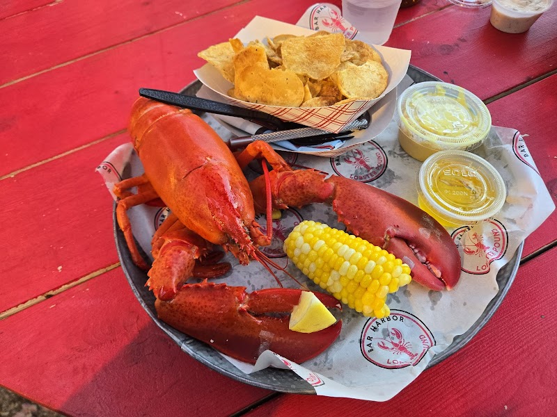 Red lobster on a metal tray with corn on the cob, chips, lemon wedge and sauces at Acadia National Park.