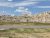 Badlands National Park landscape with layered sandstone formations rising behind a grassy plain and road near the visitor area.