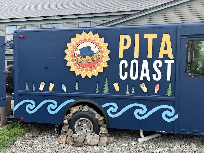 Blue food truck with a yellow sunburst emblem, turquoise wave decals, and small icon illustrations beside rocky ground, Acadia National Park.