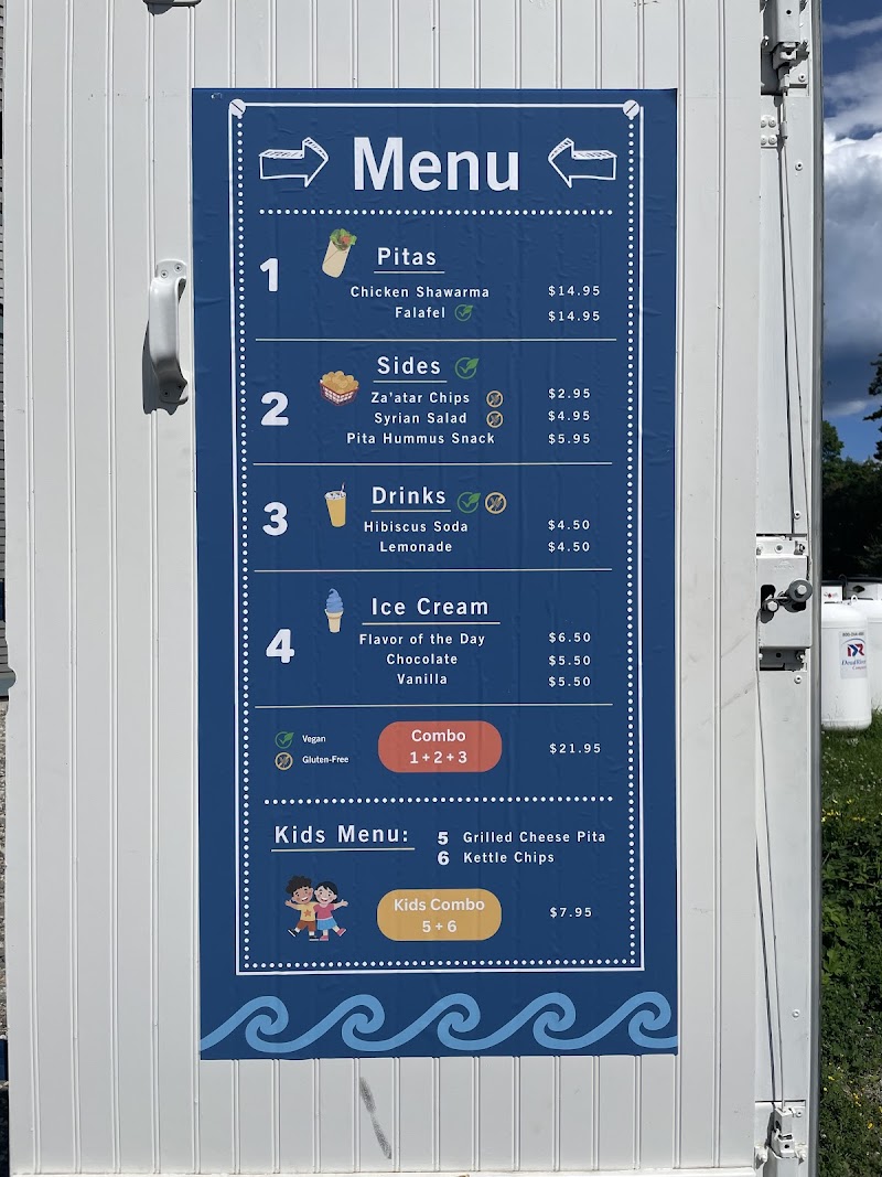 Blue menu board on a trailer shows Pitas, Sides, Drinks, Ice Cream with prices; located at Acadia National Park.