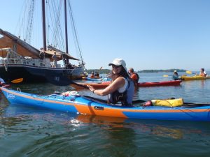 Castine Harbor kayak scene in Acadia National Park, with a colorful tandem kayak beside a tall-masted ship.