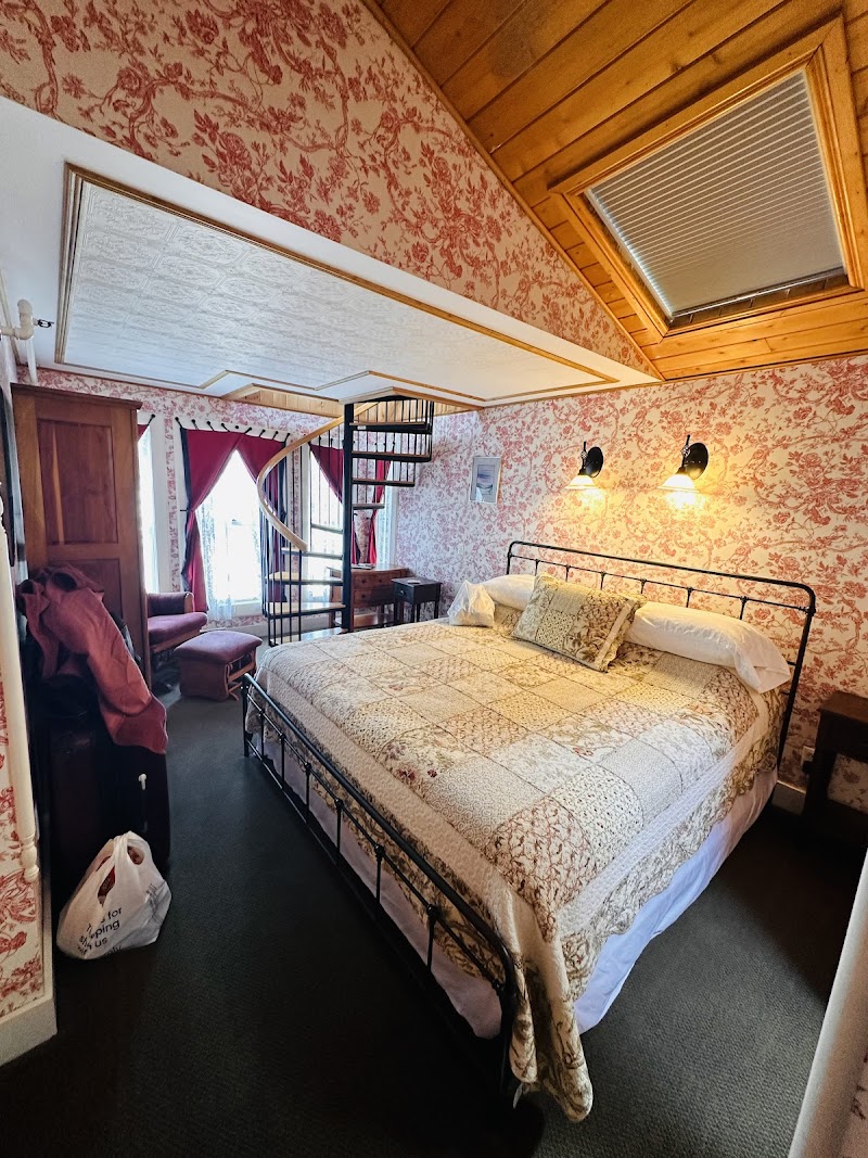 Cozy bedroom in Acadia National Park with a wrought iron bed, patchwork quilt, red floral wallpaper, wooden ceiling, skylight and a spiral staircase.