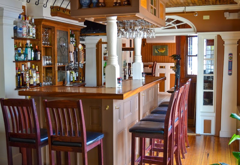 Cozy pub bar with a polished wood counter, high wooden stools, hanging glassware, and bottle shelves in Acadia National Park.