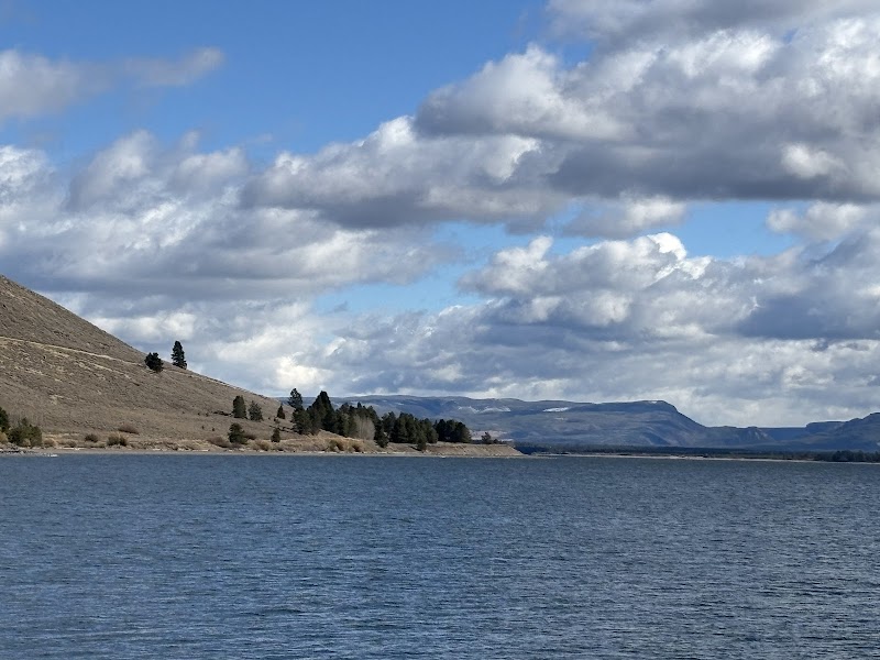 Hebgen Lake widens under a cloudy sky, with a sloping hillside and scattered pines along the shore in Yellowstone National Park.