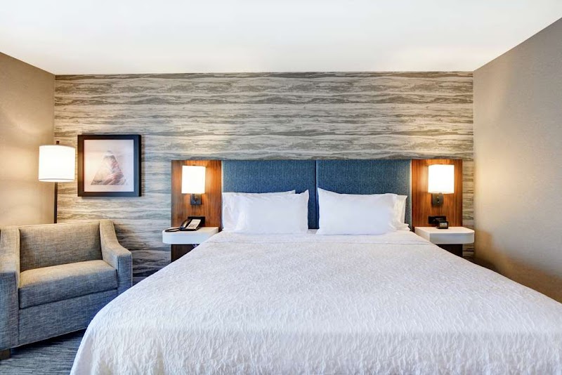 Modern hotel room with a large bed, white bedding, blue headboard, two nightstands with lamps, a gray chair, and framed art in Arches National Park.