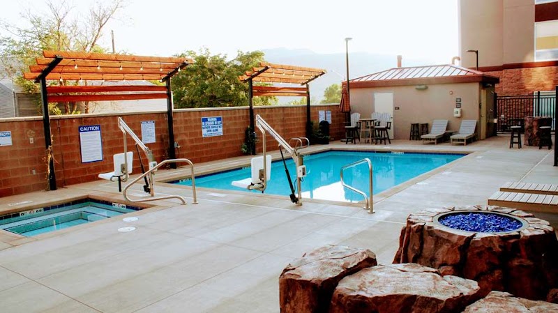 Pool area with a rectangular pool, hot tub, lounge chairs, and shaded pergolas beside a lodge at Arches National Park.