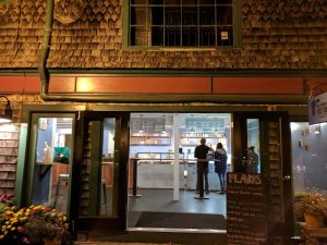Acadia National Park shop with shingled exterior; glass doors open to interior where two customers stand at the counter.