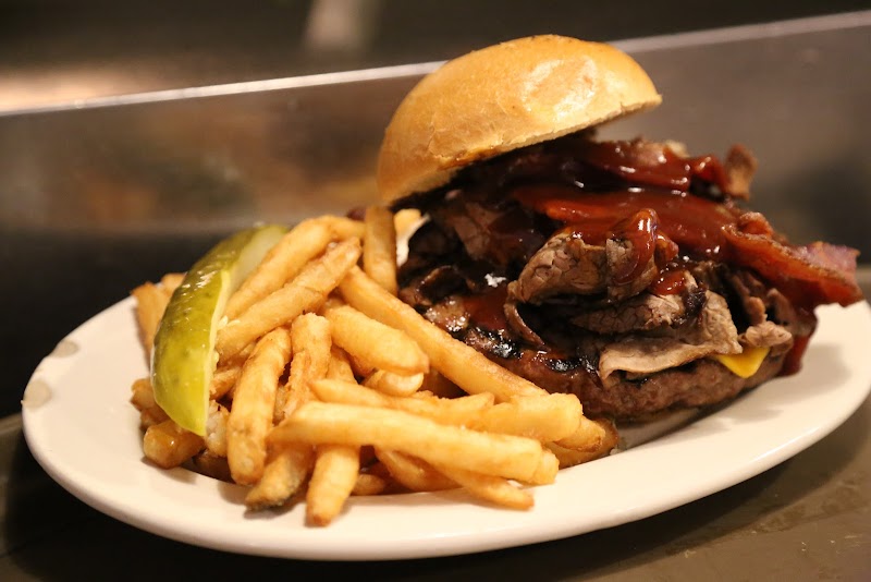 Juicy burger topped with onions and barbecue sauce, served with fries and a pickle at Arches National Park.