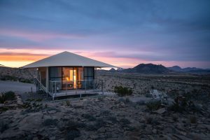 Desert lodging cabin at Big Bend National Park sits on a rocky plain under a colorful desert sunset.