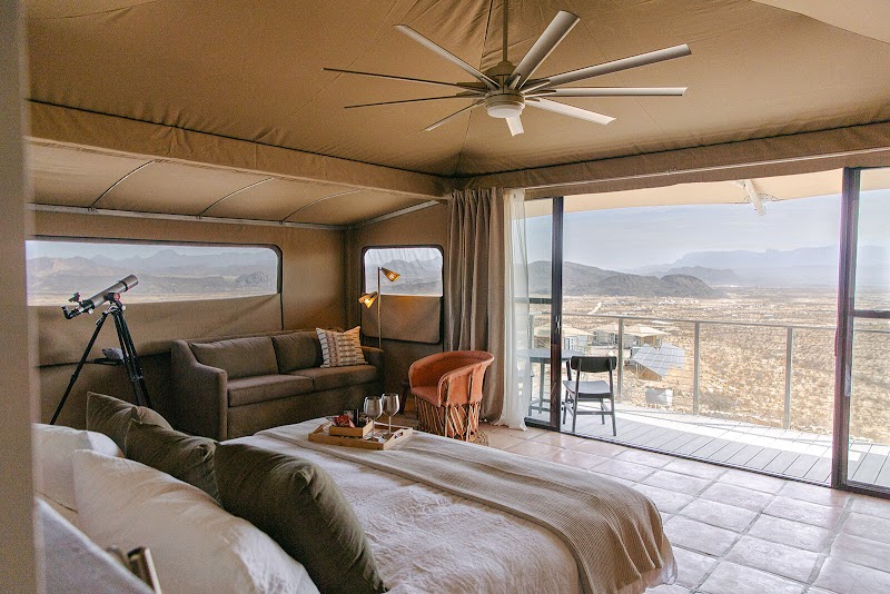 Interior of a desert retreat room in Big Bend National Park with a telescope, lounge seating, and a wraparound balcony overlooking rugged desert.
