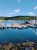 Boats docked along a calm harbor at Acadia National Park, blue water reflecting masts against forested hills.