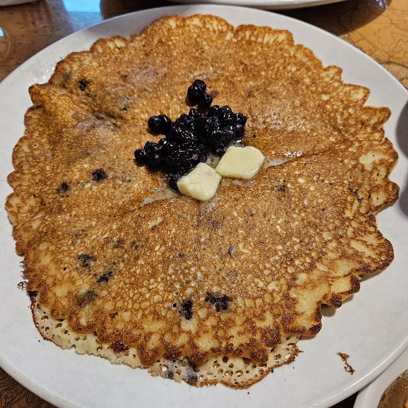Golden brown blueberry pancake with visible berries, topped with blueberries and two pats of butter on a white plate in Acadia National Park.